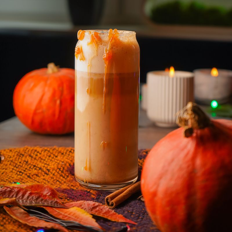 Kawa Pumpkin Iced Latte z syropem waniliowym. Jesienne dekoracje, kolorowe liście, laski cynamonu, świece i dynie dekoracyjne.