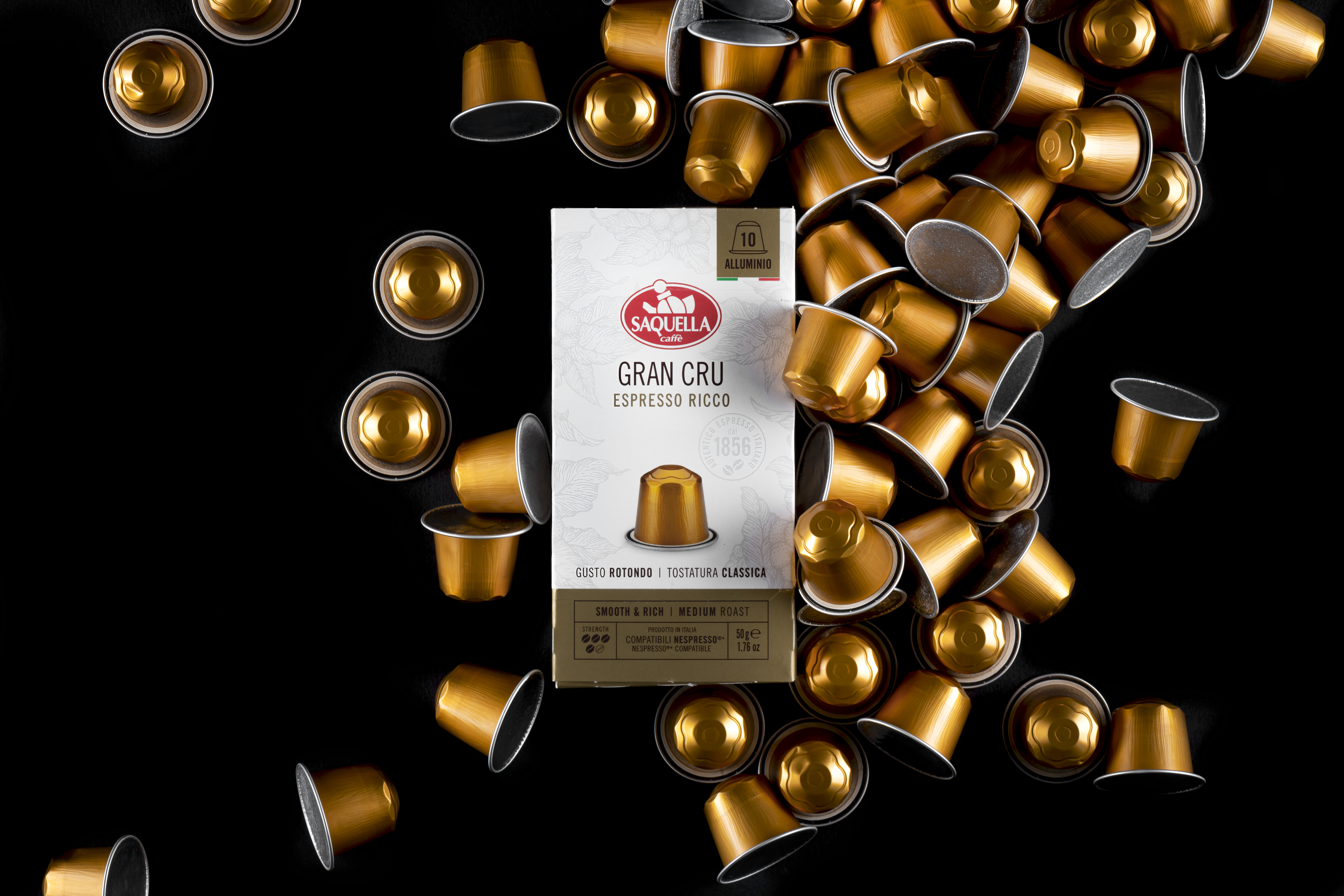 Eleganckie, złote kapsułki z kawą Saquella Gran Cru Espresso Ricco na czarnym tle – przykład wysokiej jakości włoskiej kawy do ekspresów kapsułkowych, idealnej do nowoczesnego biura, które stawia na komfort, wygodę i prestiż.