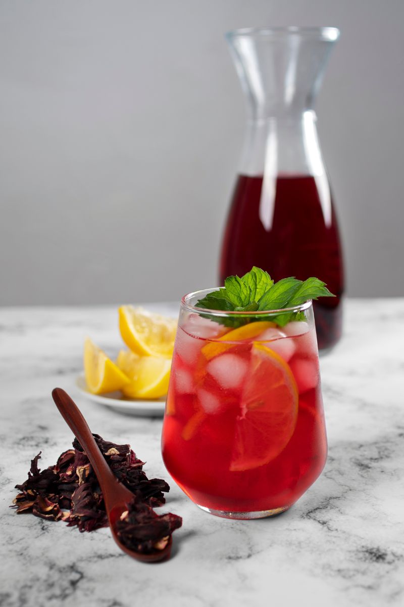 Lemoniada hibiskusowa z cytryną, miętą i dużą ilością lodu, podana wprzezroczystej szklance.