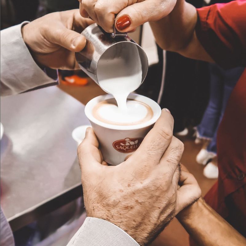 Przygotowanie cappuccino italiano. Wlewanie kremowego, spienionego mleka do kawy.