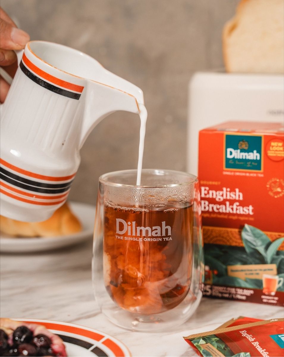 Dodawanie mleka do herbaty Dilmah English Breakfast Tea. W tle widoczne opakowanie herbaty śniadaniowej.