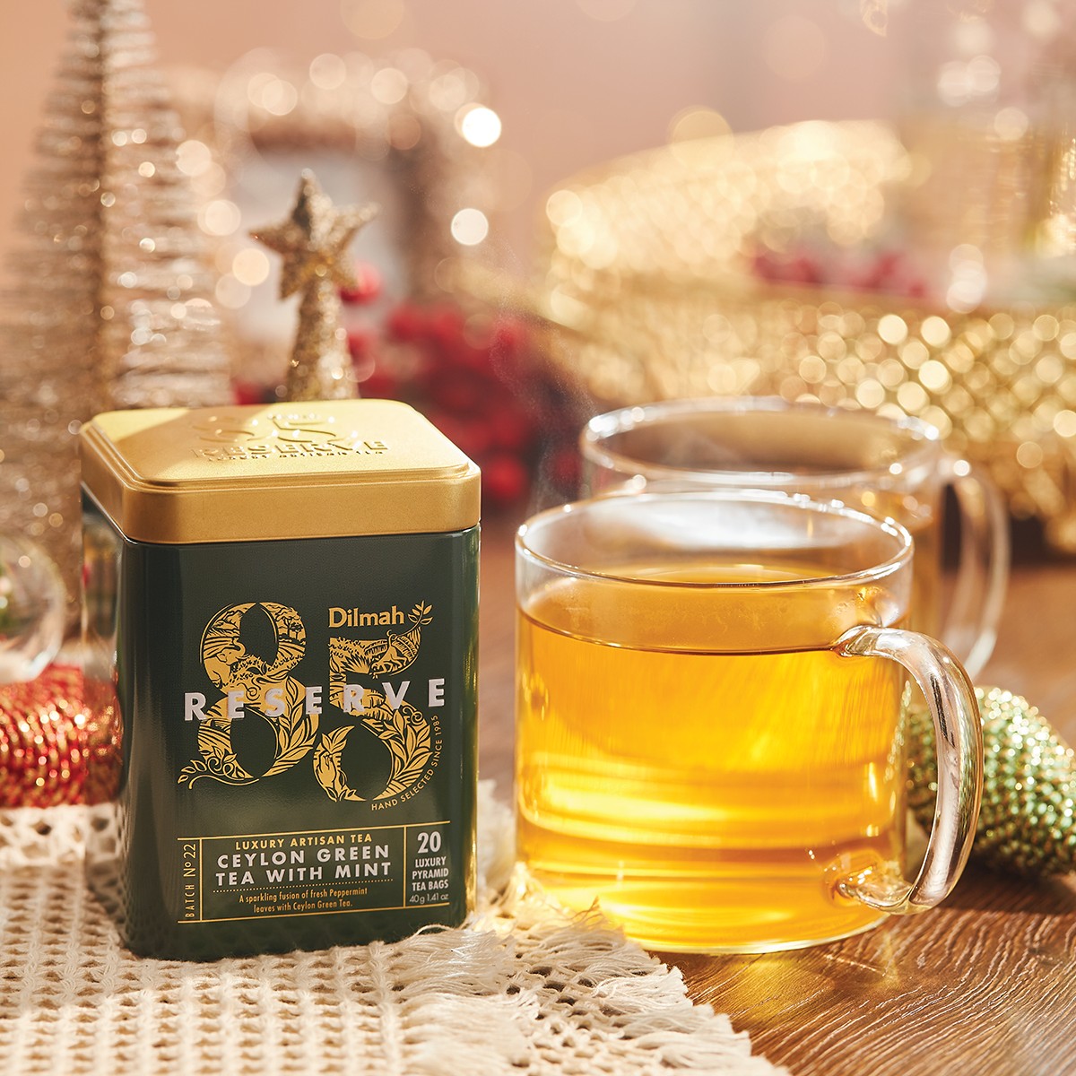 Herbata na prezent dla szefa Dilmah Ceylon Green Tea with Mint. Obok kubek z zieloną herbatą i dekoracje świąteczne.