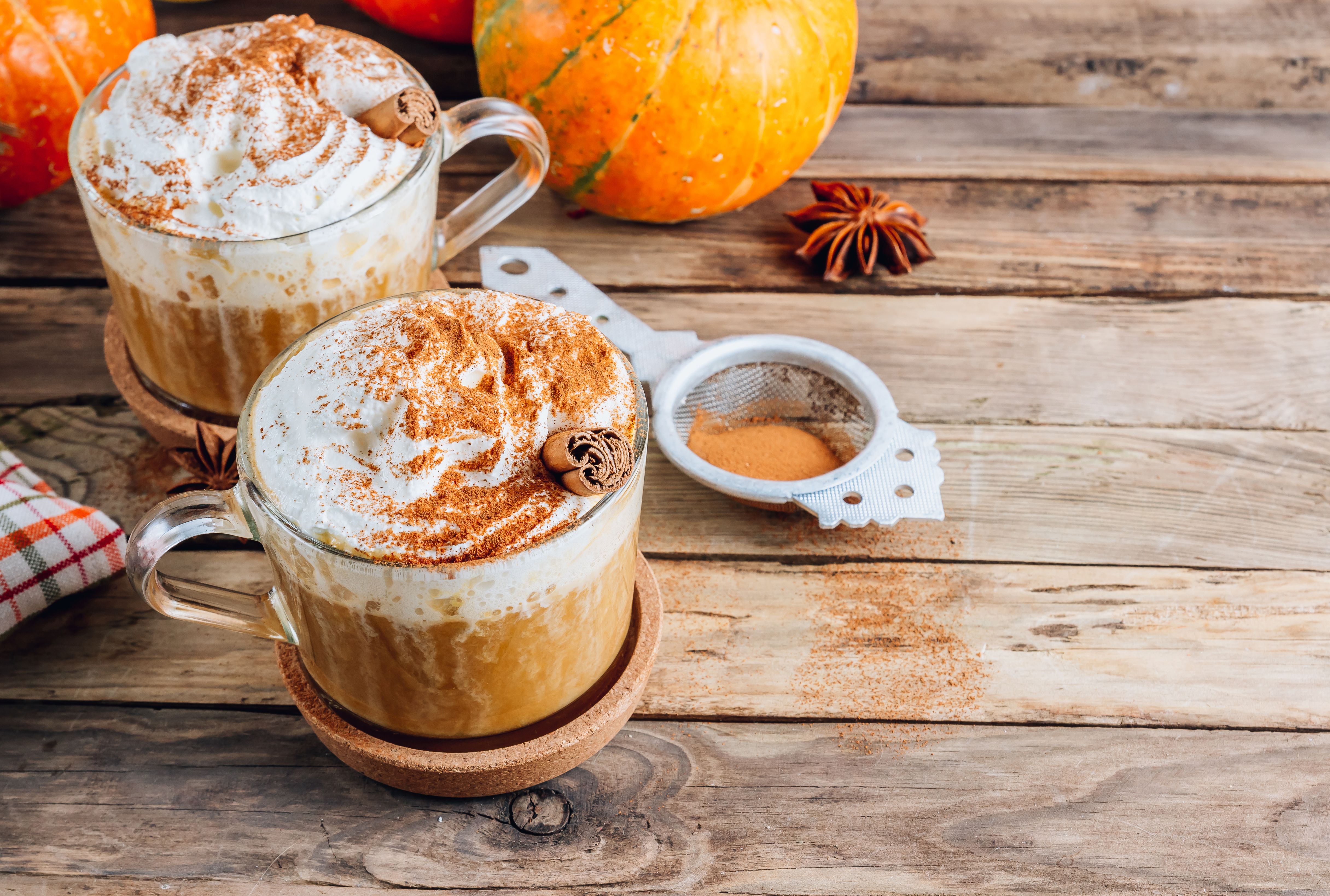 Dwa kubki z jesienną dyniową kawą cappuccino udekorowane bitą śmietaną i cynamonem.