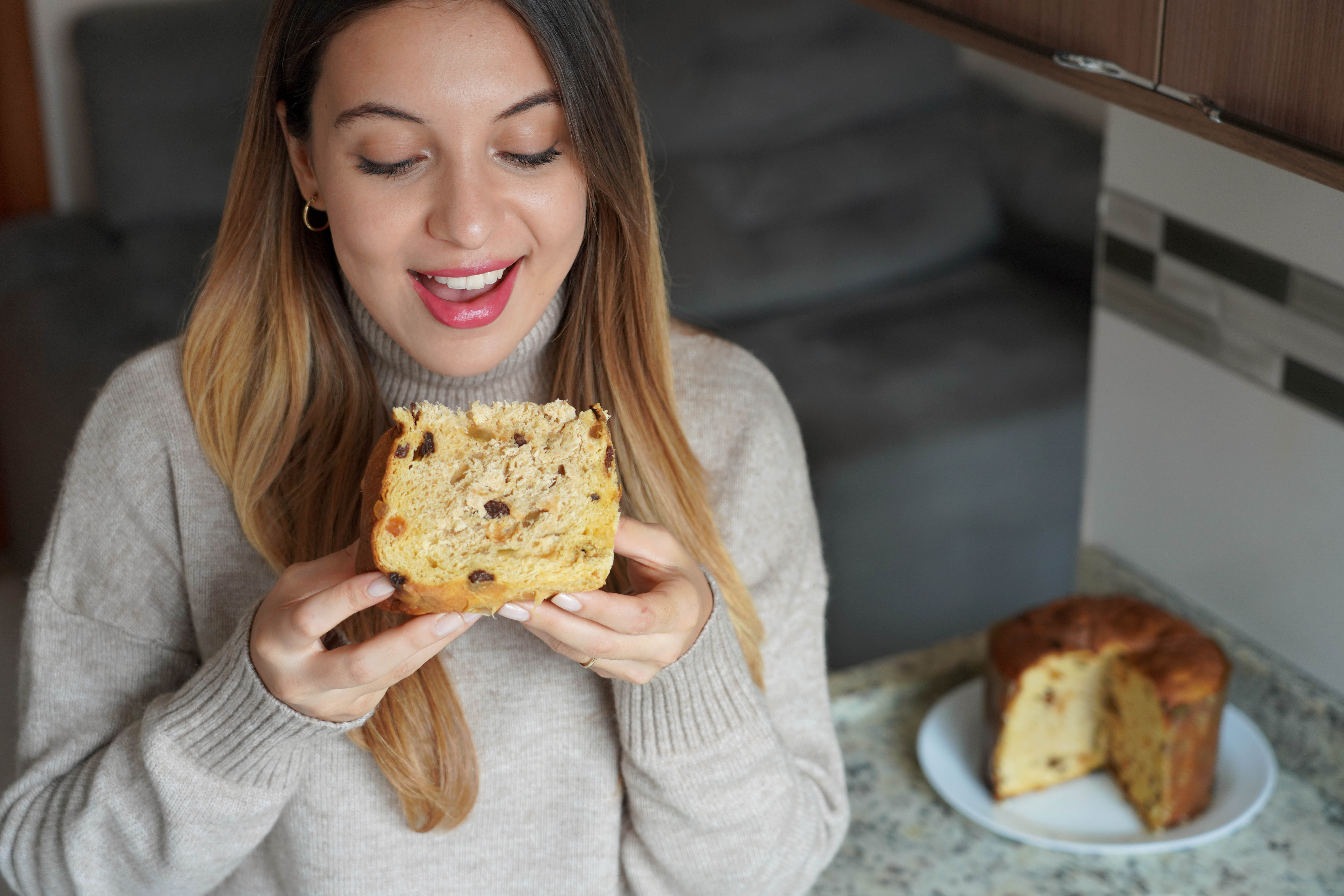 Uśmiechnięta kobieta degustuje włoski wypiek z bakaliami – Panettone.