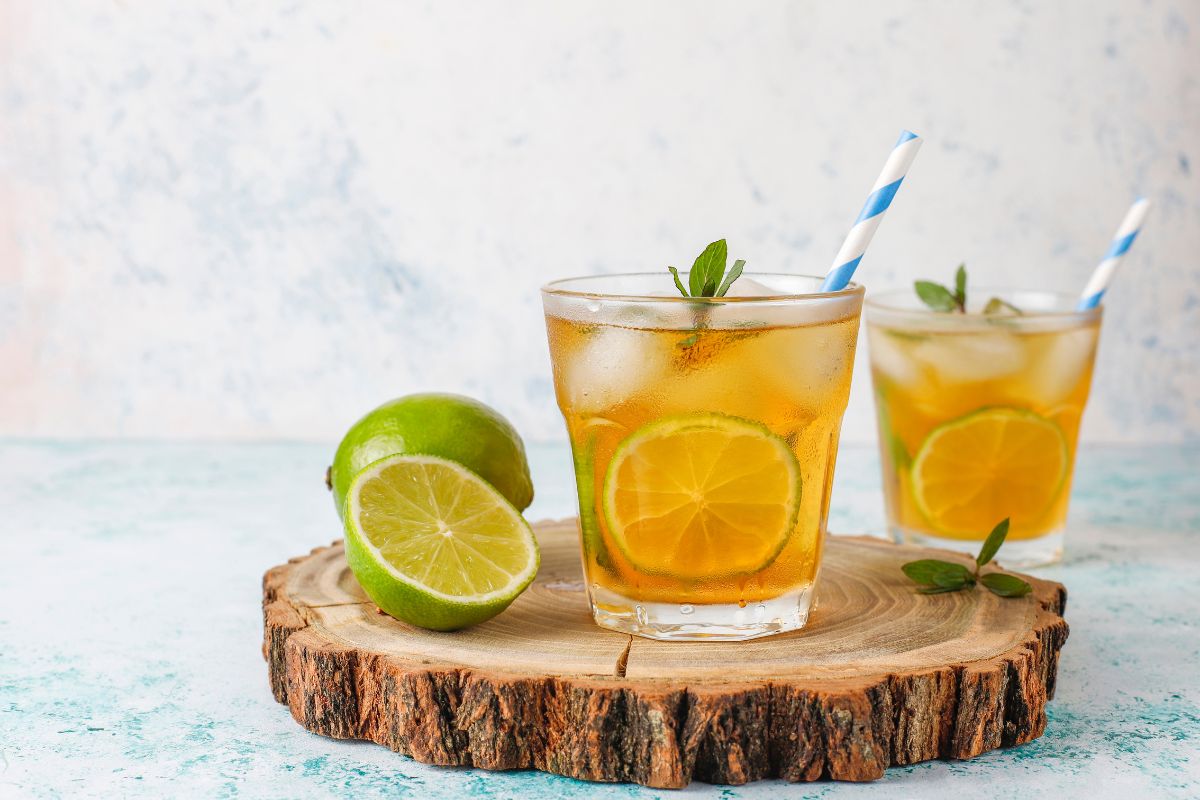 Napój na upały z mięty i limonki a’la mojito w dwóch szklankach, przyozdobionyplastrami cytrusa, lodem i świeżą miętą.