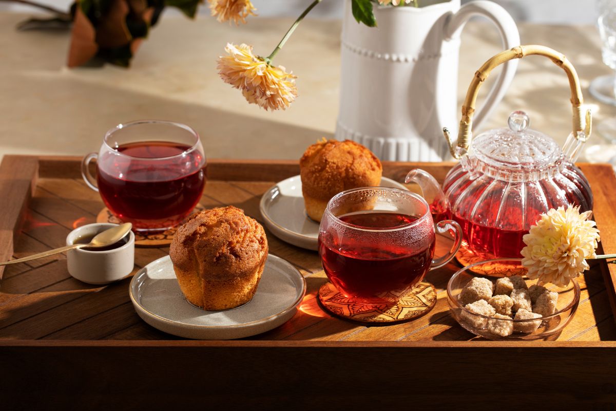 Herbata Dilmah English Afternoon Tea w przezroczystym dzbanku, dwie filiżanki i babeczki na tacy śniadaniowej.
