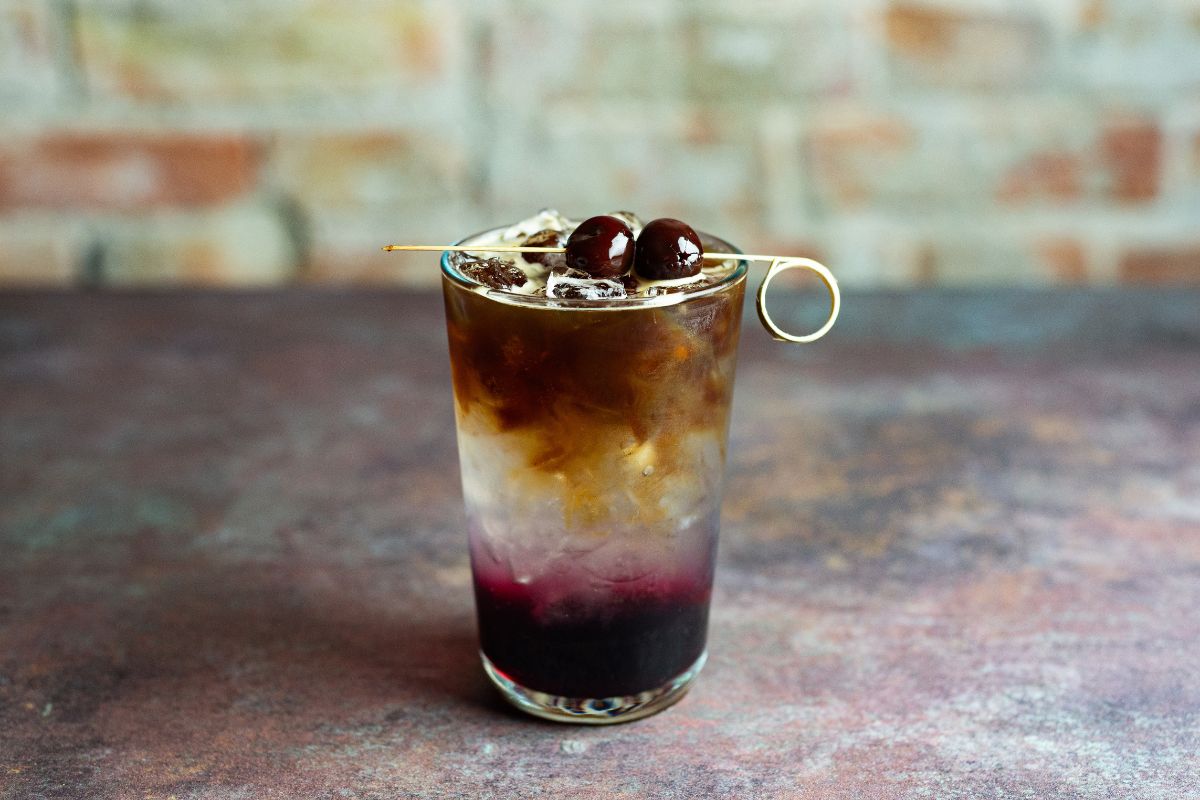 Cherry espresso tonic z lodem i dekoracją z wiśni kandyzowanych w przezroczystej szklance.