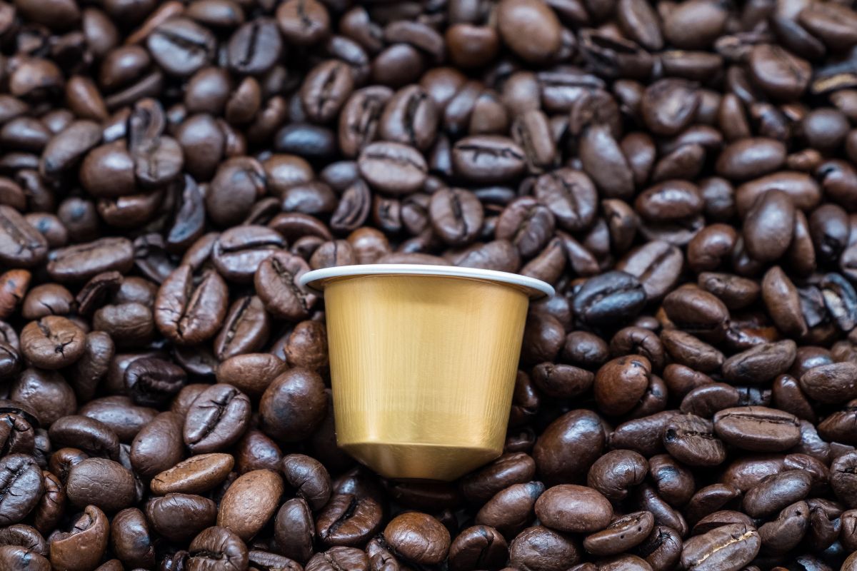 Złota kapsułka Saquella Gran Cru Espresso Ricco 100% arabika na tle ziaren kawowych.