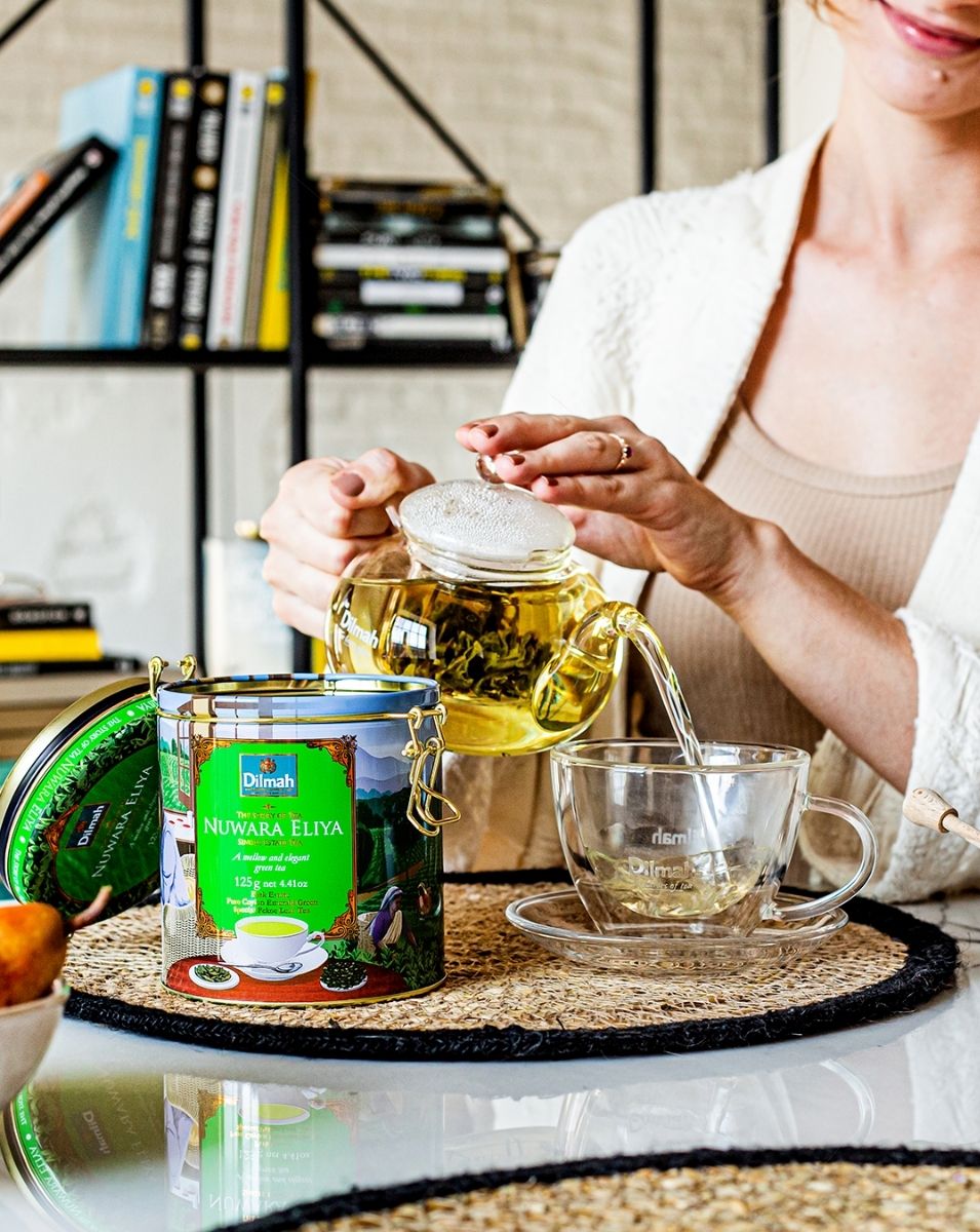 Uśmiechnięta kobieta nalewająca do filiżanki świeżo zaparzoną, aromatyczną zieloną herbatę single estate Dilmah Nuwara Eliya.
