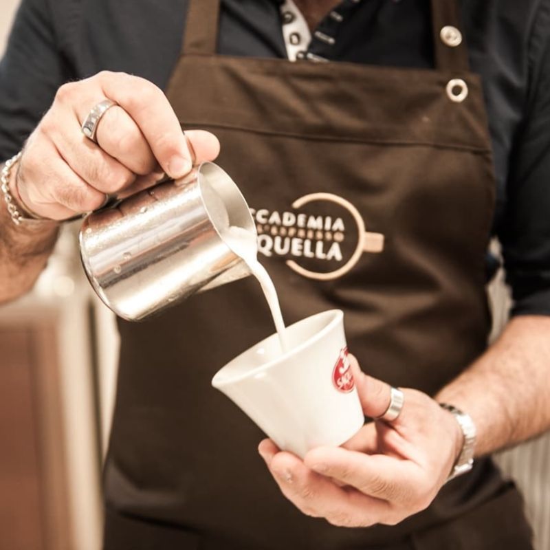 Barista akademii Saquella w trakcie przygotowywania kawy ze spienionym mlekiem.