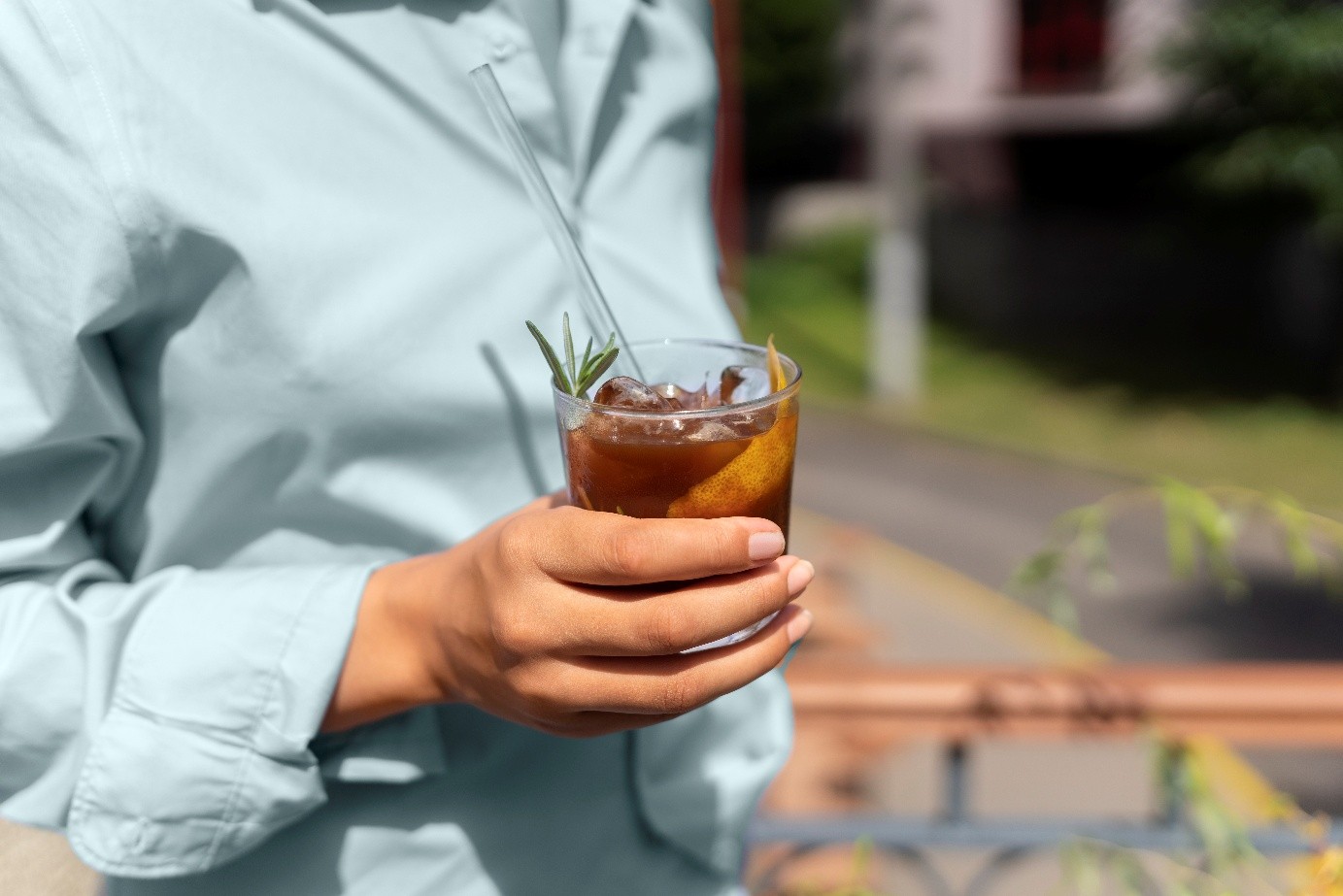Kobieta trzymająca espresso romano w przezroczystej szklance. Napój ozdobiony jest skórką pomarańczową i gałązką rozmarynu.