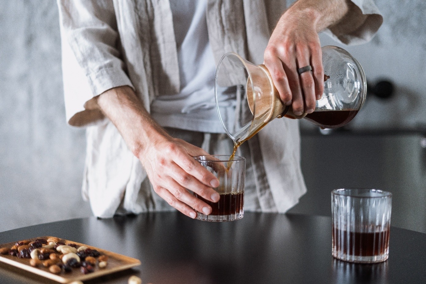 Mężczyzna nalewa cold brew z drippera do ozdobnych szklanek. Kawa ma ciemny, nasycony kolor.