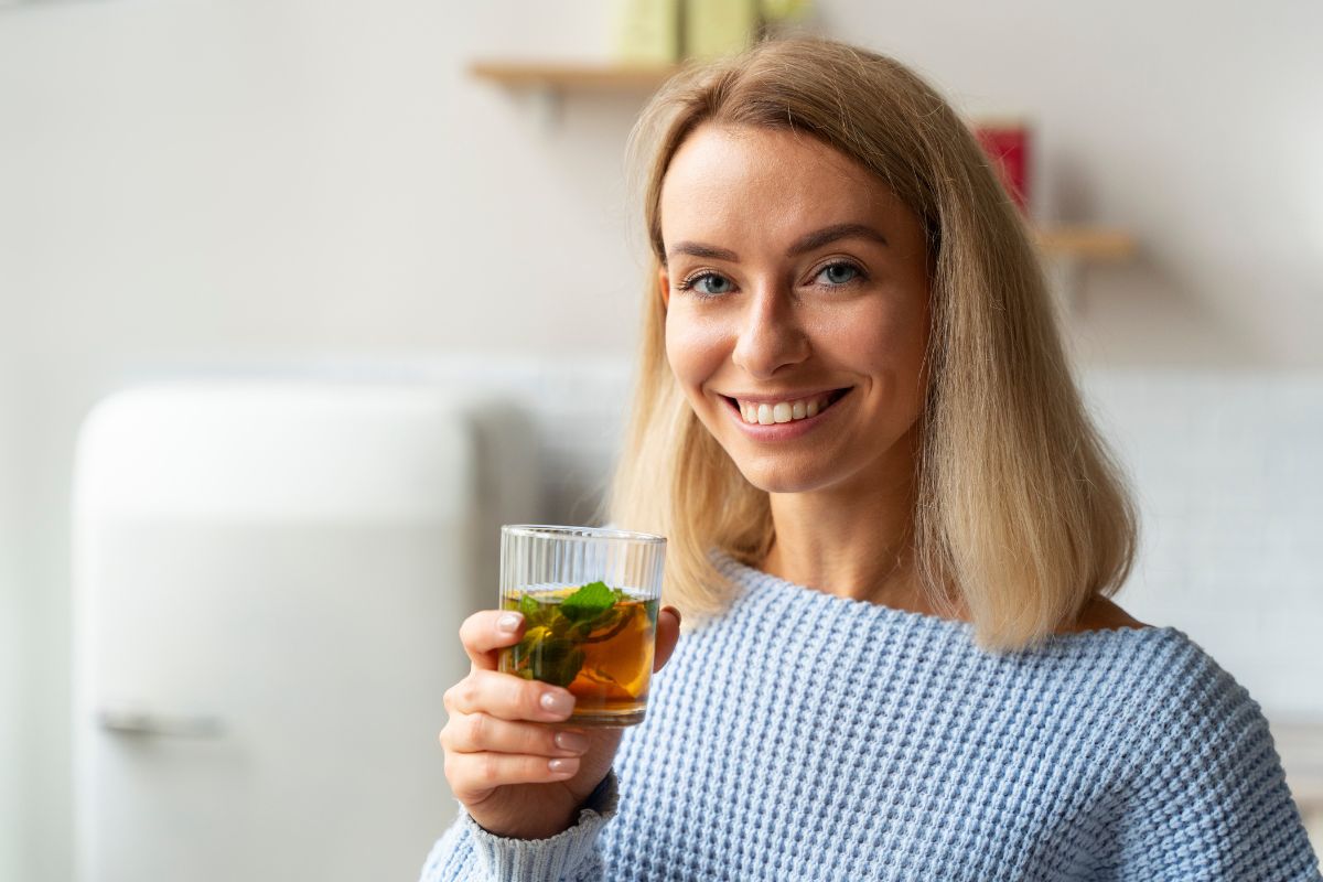 Uśmiechnięta kobieta pijąca czarną herbatę Dilmah z dodatkiem cytryny i mięty.
